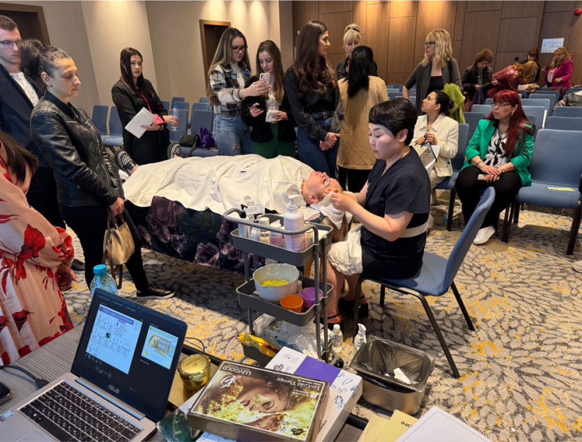 Facial skincare demonstration observed by attendees — April 2025 seminar in Bulgaria; third photograph from the official composite.