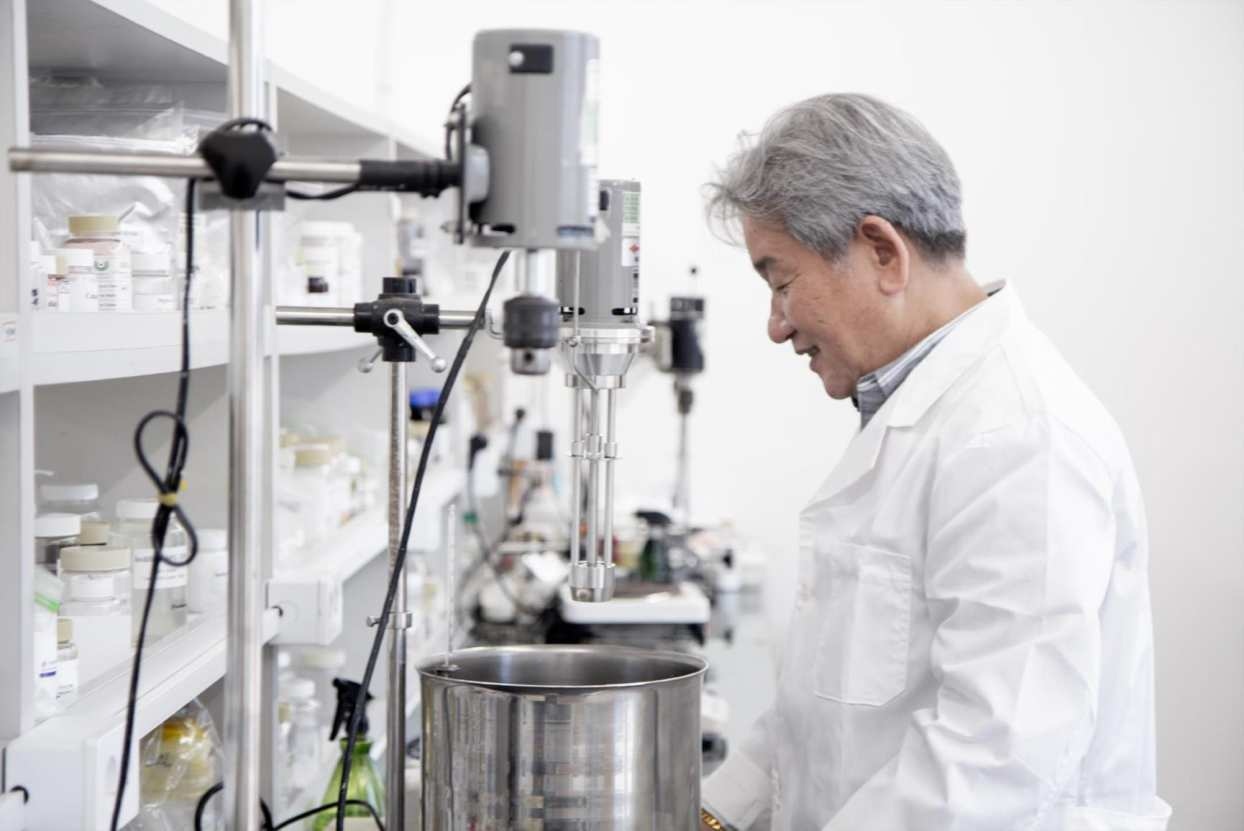 Researcher in a white coat working with cosmetic formulation equipment — official HYUNJIN C&T company profile, page 19